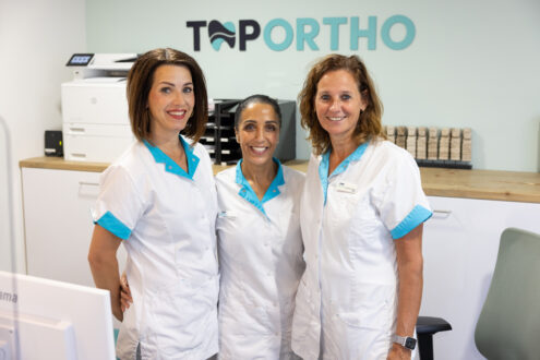 Twee receptiemedewerkers en een orthodontie assistent poseren achter de receptie van TopOrtho Nieuwegein